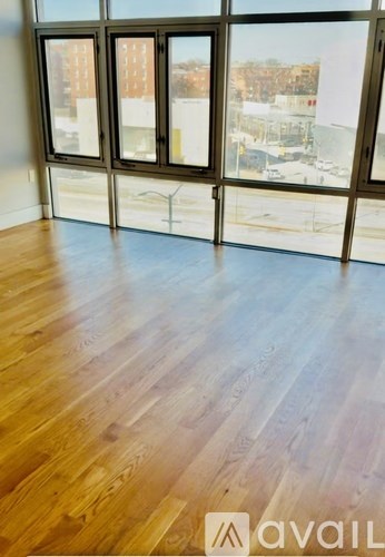 A room with wooden floors and large windows overlooking a parking lot.