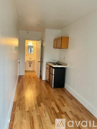 A long hallway with wooden floors and a kitchen area with a fridge and a stove.