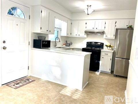 A kitchen with white cabinets and appliances, a sink, and a refrigerator.