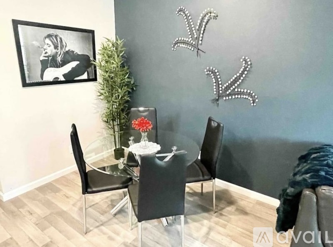 A dining room with a glass table and chairs, a plant, and a framed picture on the wall.