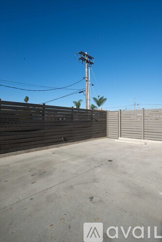 A clear blue sky meets a concrete ground with a wooden fence and a metal pole with wires.