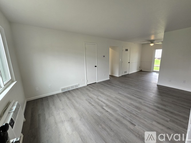 A spacious room with wooden flooring and white walls.