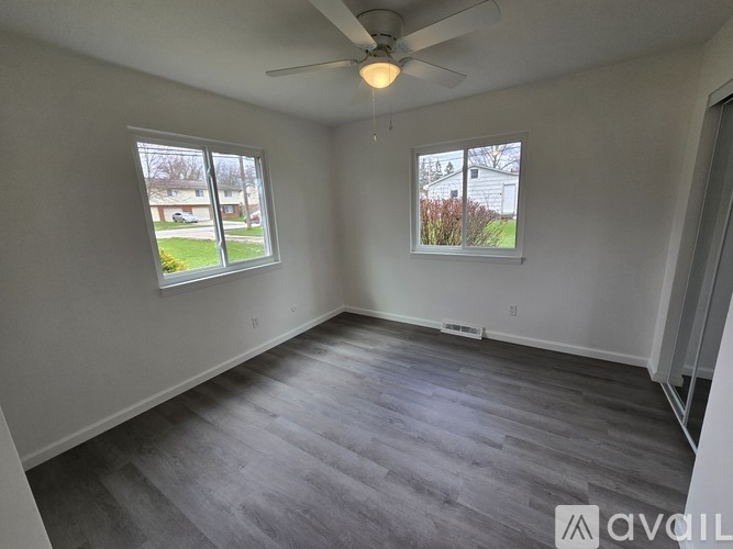 A room with a ceiling fan and two windows.