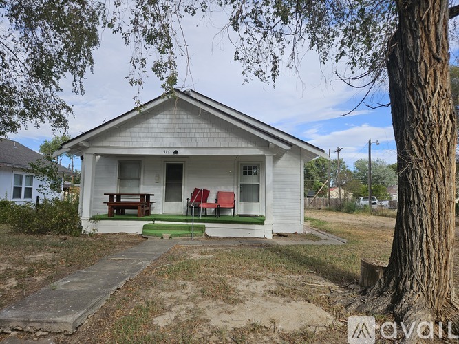 A small white house with a porch and a tree in front.