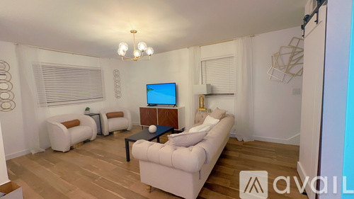 A living room with a white couch, a wooden coffee table, and a television on the wall.