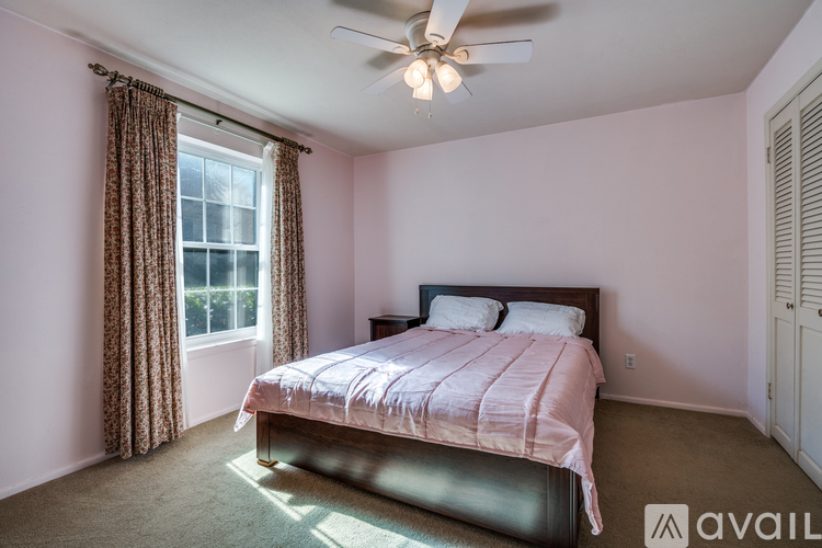 A bedroom with a bed, a window with curtains, and a ceiling fan.