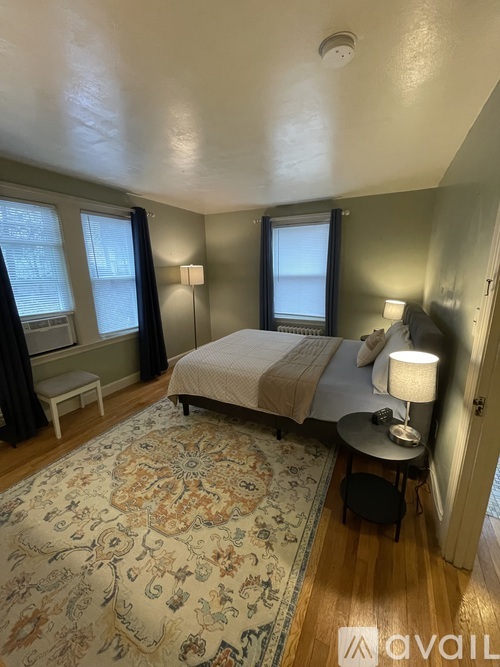 A bedroom with a bed, a table with a lamp, and a window with curtains.