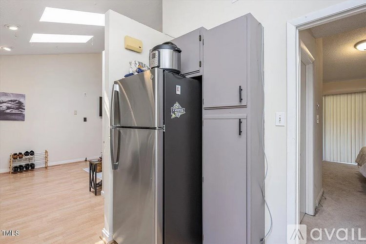 A large stainless steel refrigerator with a black door is in a room with wooden flooring and a white wall.