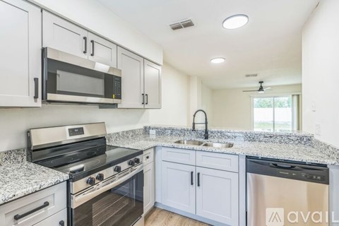 A kitchen with a black stove top oven, a black microwave, a granite counter top, and white cabinets.