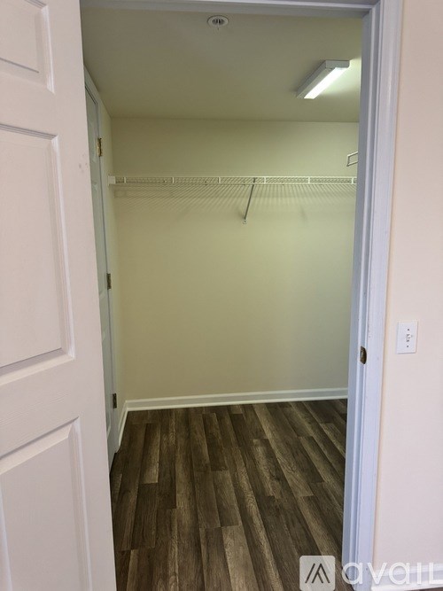 A white door opens to a room with a wood floor and a white wall.