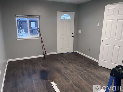 A room with a white door and a window with a red broom leaning against the wall.