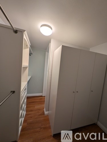 A white refrigerator is in a kitchen with wood floors and white cabinets.