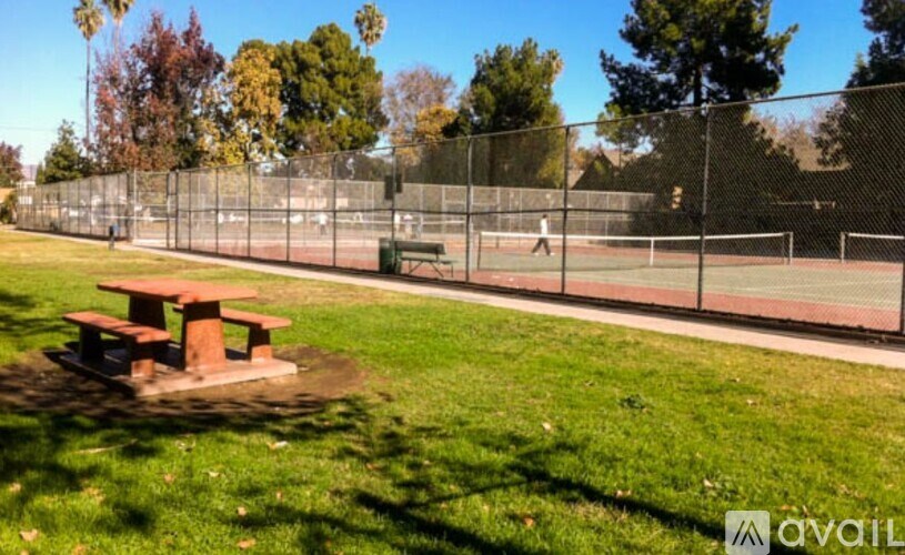A tennis court is surrounded by a fence and there is a picnic table in the foreground.