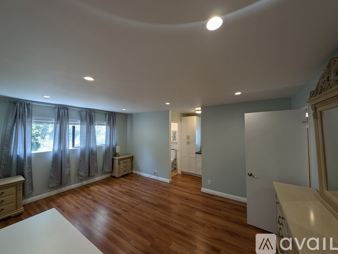 A spacious room with wooden floors and a large window with curtains.