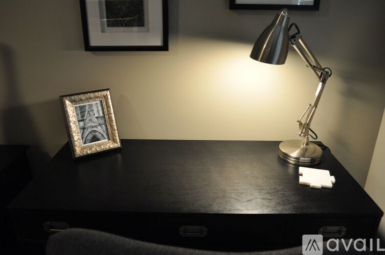 A desk with a lamp, picture frame, and a small white object on it.