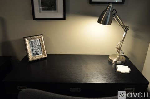 A desk with a lamp, picture frame, and a small white object on it.