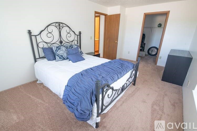 A bed with a black metal headboard and a blue blanket is in a room with a carpeted floor.