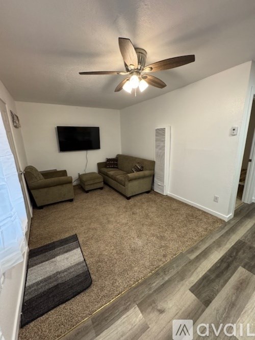 A living room with a ceiling fan and a flat screen TV mounted on the wall.
