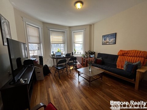A living room with a black couch, a wooden floor, and a television.