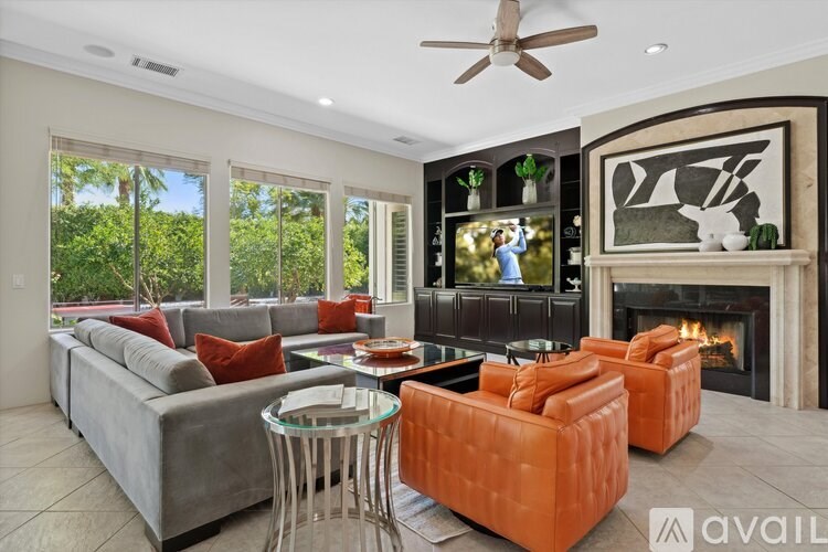 A living room with a grey couch, orange ottoman, and a fireplace.
