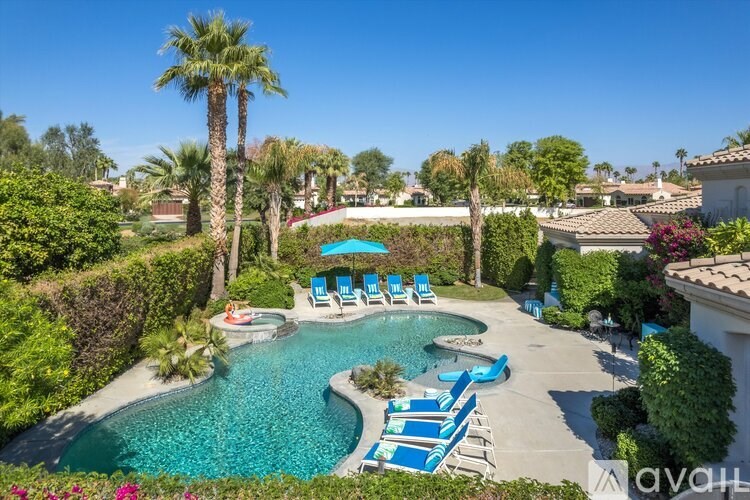 A pool surrounded by palm trees and blue lounge chairs.