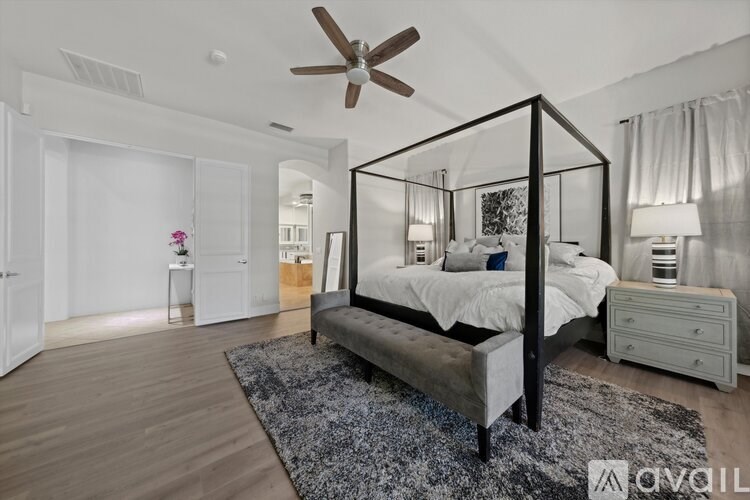 A bedroom with a four poster bed, a bench and a ceiling fan.