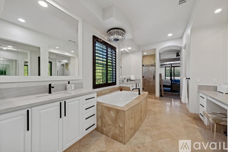 A large, well-lit bathroom with a marble tub and double sinks.