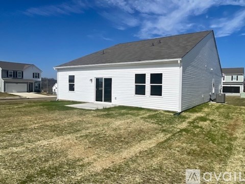 A white barn-like building with a grey roof and a black door is situated in a grassy field.