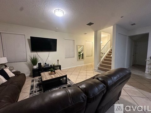 A living room with a brown leather couch and a flat screen TV mounted on the wall.