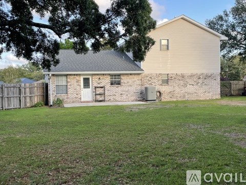 A house with a beige siding and a grey roof is surrounded by a grassy area and a wooden fence.