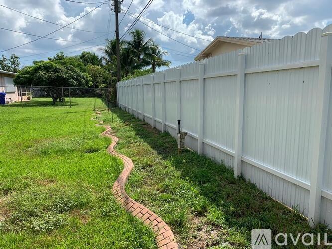 A white fence runs along a grassy area with a brick path.