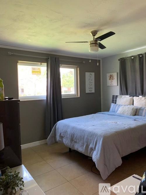 A bedroom with a bed, a ceiling fan, and a window with curtains.