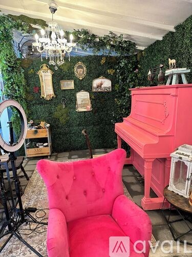 A pink chair sits in front of a pink piano in a room with a green wall.