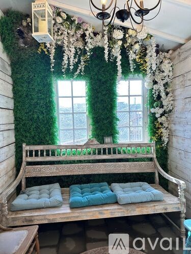 A wooden bench with blue cushions is in front of a window with greenery.