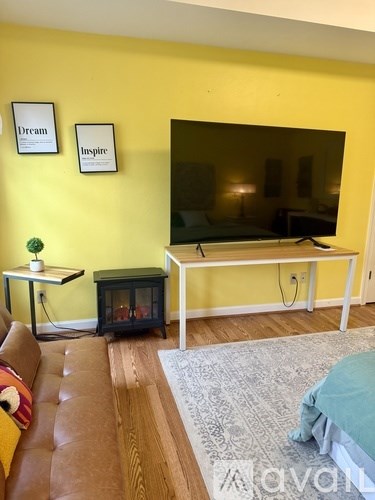 A living room with a brown leather couch, a grey rug, a black table, a white TV stand, and two framed pictures on the wall.