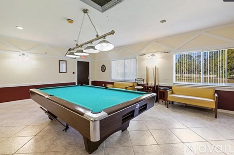 A pool table in a room with a bench and a window.
