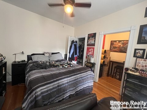 A bedroom with a bed, a ceiling fan, and a chair.