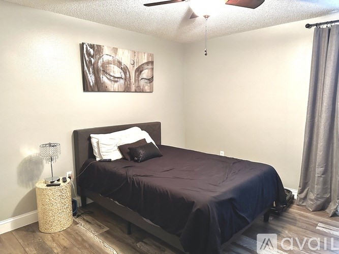 A bedroom with a bed, pillows, a nightstand with a lamp, and a painting on the wall.