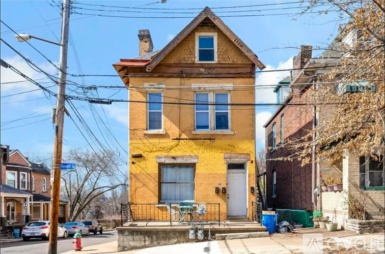 A yellow house with a red roof is in front of a blue street sign.