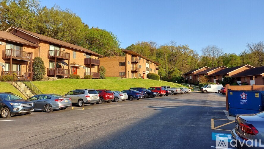 A row of cars parked in a parking lot in front of apartment buildings.