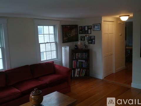 A red couch sits in a living room with a bookshelf and pictures on the wall.
