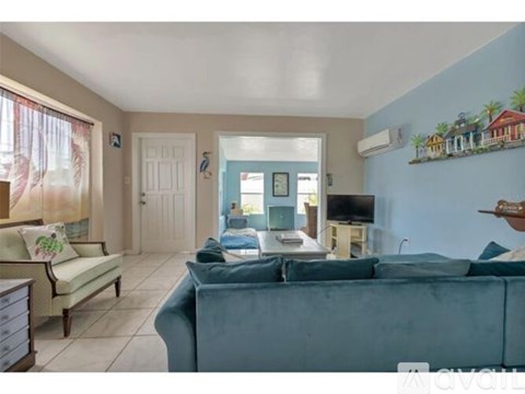 A living room with a blue couch and a painting of a house on the wall.
