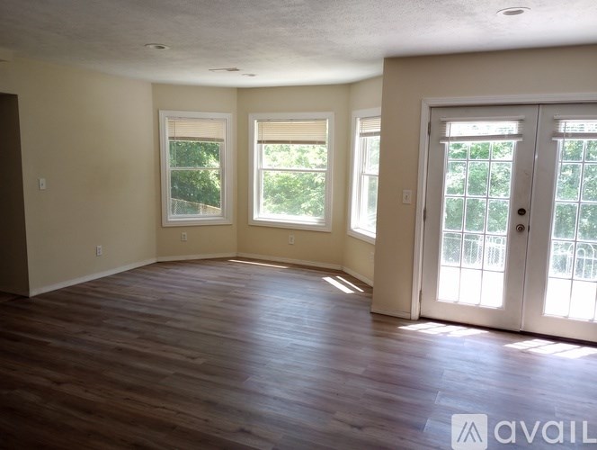A spacious room with wooden floors and three windows.