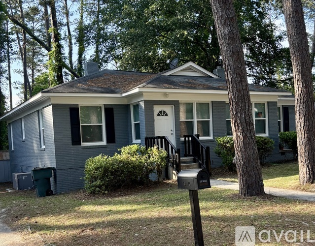A house with a grey exterior and a white door is surrounded by trees.