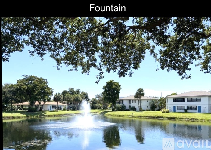 A fountain in the middle of a pond surrounded by trees and houses.
