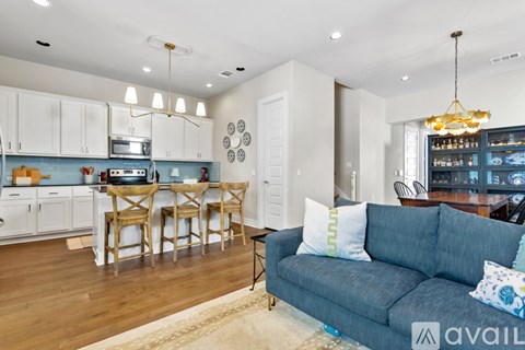 A living room with a grey couch and a kitchen area in the background.
