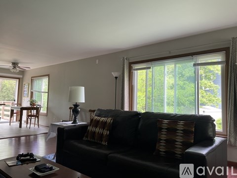 A living room with a black couch and a table with a lamp on it.