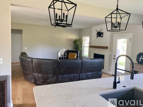 A living room with a black leather sofa and a kitchen area with a sink.