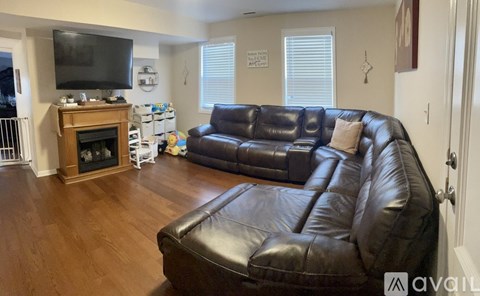 A black leather couch in a living room with a television and fireplace.
