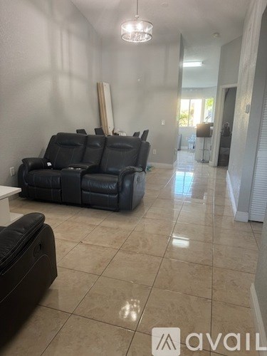 A living room with a large black leather couch and a tiled floor.